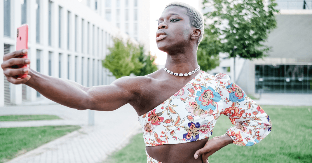 Existir fora do binário: Uma pessoa não binária de pele negra, posando para uma selfie em um ambiente externo com árvores ao fundo.